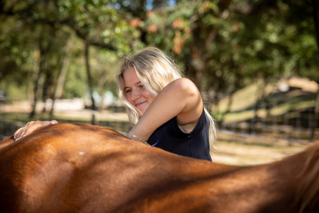 Carla sourit derrière le dos d'un cheval alezan